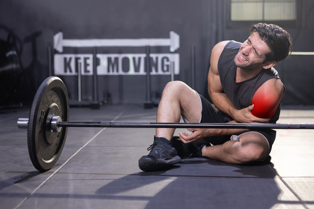 Person experiencing shoulder pain while lifting weights in a gym.